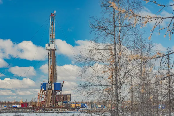 Winter landscape of an oil and gas field with a drilling rig and special equipment in the polar forest tundra. Ground is covered with snow