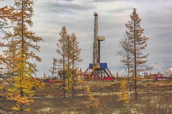 Landscape of an oil and gas field in the northern forest-tundra of Siberia. The main object is a drilling rig that blends into the picturesque autumn landscape of taiga trees