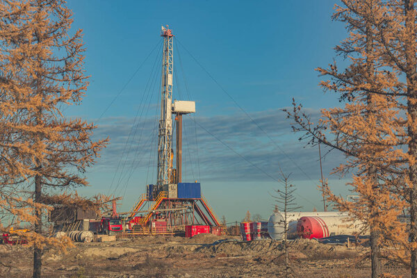 Landscape of an oil and gas field in the northern forest-tundra of Siberia. The main object is a drilling rig that blends into the picturesque autumn landscape of taiga trees