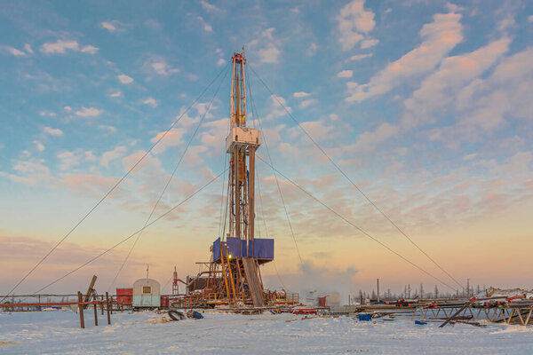 Drilling wells in the winter at an oil and gas field in the Arctic. Polar day with textured beautiful sky. Steam puffs for heating equipment