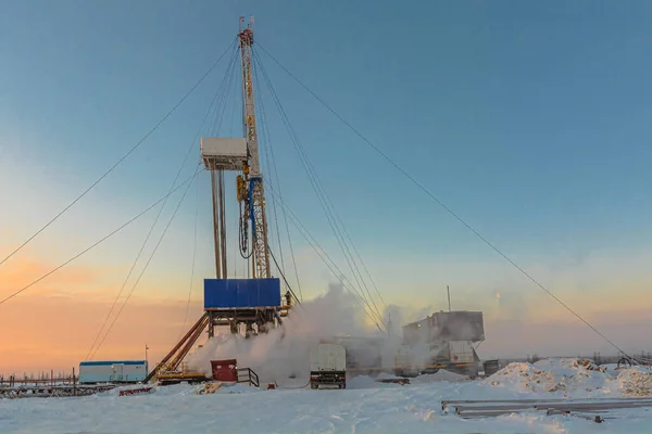 Drilling wells in the winter at an oil and gas field in the Arctic. Polar day with textured beautiful sky. Steam puffs for heating equipment