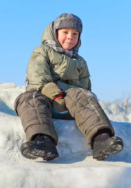 Menino sorridente sentado na neve — Fotografia de Stock