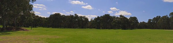 Panorama of green grass on empty rest area surrounded by trees and clouds on blue sky in Breaside Park, Victoria, Australia