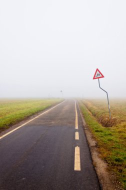 tehlike işareti ile boş kırsal yol üzerindeki sis