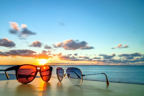 在日落时的热带海滩桌上的太阳镜 — 图库照片