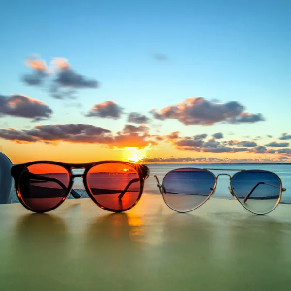 Sunglasses on tropical beach table at sunset — Stock Photo, Image