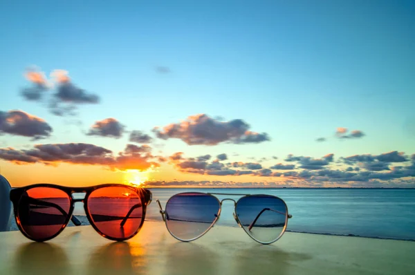 Zonnebril op tropisch strand tafel bij zonsondergang — Stockfoto