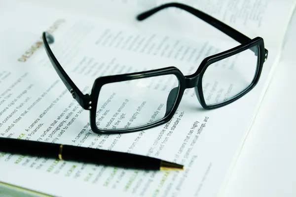Glasses and a pen on a book Stock Image