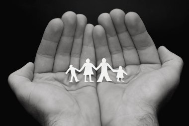 Aile kavramı. Erkek eller kağıt aile kesimini, koruyucu aileyi, geleneksel değerleri, aile korumasını, izolasyon kavramını elinde tutar. Siyah beyaz fotoğraf.