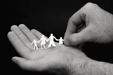 Family concept. Male hands are holding paper figures of a family. Foster family, traditional values, family protection concept. Black and white photo. clipart