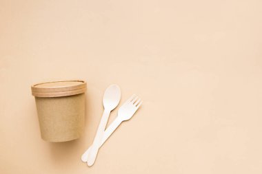 Bej arka planda tahtadan çatal ve kaşıkla tek kullanımlık kağıt bardak. Doğal malzemeden çevre dostu tek kullanımlık sofra takımı. Asgari konsept.