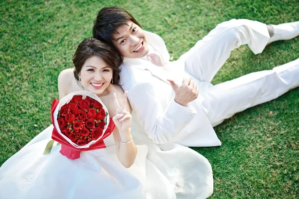 Porträt von Braut und Bräutigam auf frischem Gras sitzend mit Rosenbou — Stockfoto
