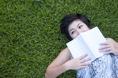 Genç bir kadın parkta kitap okuyor.