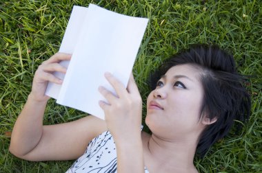 Genç bir kadın tarlada kitap okuyor.