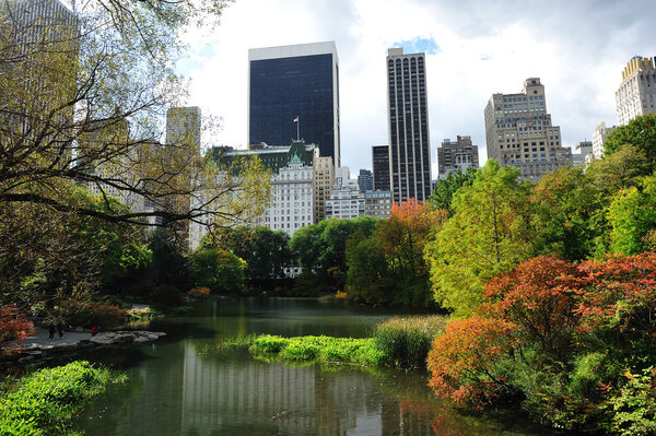 A pond at central park surrounded by tall buildings in Fall
