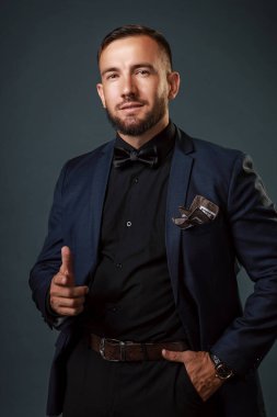 Bu, iş elbisesi ve siyah gömleği olan sakallı beyaz bir genç. Gri arkaplanda stüdyo portresi