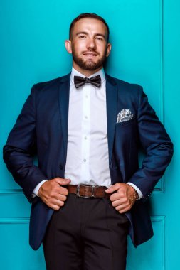 Klasik ceketli kendine güvenen bir adam ve bir kelebek duvarda durur ve gülümser. Stüdyo resmi.