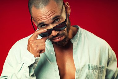 Kırmızı arka planda güneş gözlüğü altında esmer bir Latin sorgusunun portresi. Zalim sakallı adam.