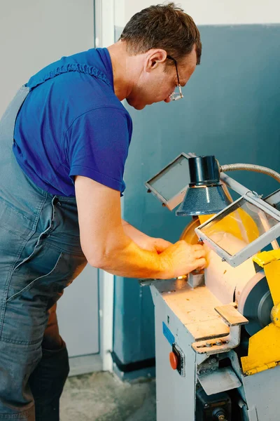 Kaukaski pracownik w mundurze wyostrza część na maszynie w pracowni. Ręczne przetwarzanie metalu. — Zdjęcie stockowe