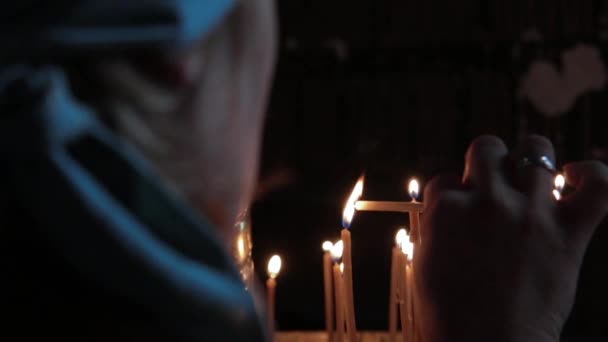 Une femme âgée met une bougie dans l'église. — Video