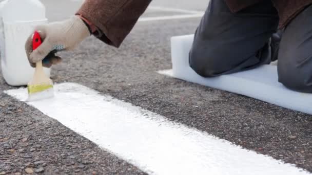 Een man schildert met een penseel op de asfaltmarkeringen voor een voetgangersoversteek. — Stockvideo