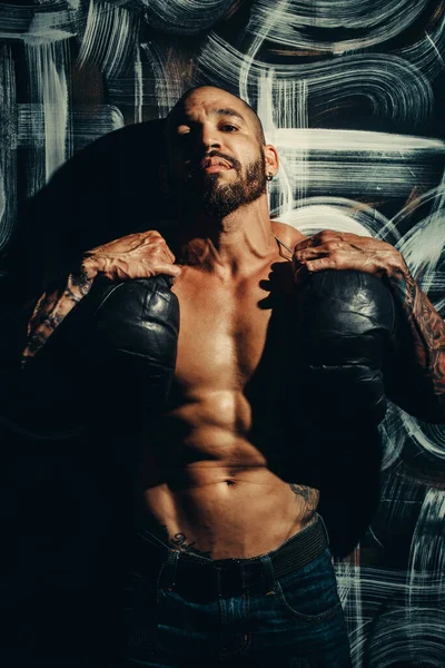 Kaslı vücutlu bir adam duvarın yanında durur ve boks eldiveni tutar. Çıplak gövdeli güçlü bir dövüşçü..