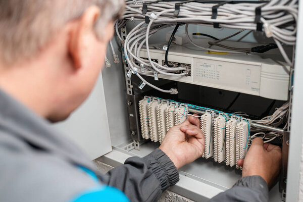 A man electrician checks the terminals of telephone communication equipment.