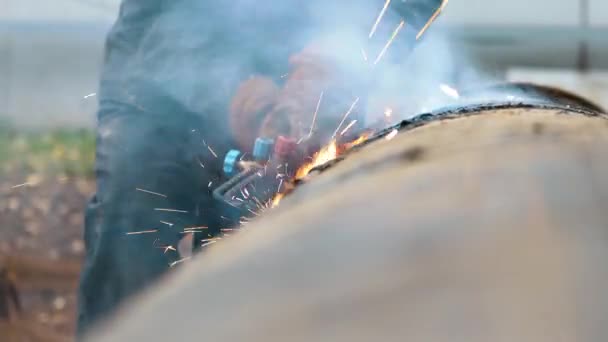 Un soldador en ropa protectora en el aire libre corta tubos de metal con soldadura de acetileno y el fuego y las chispas son visibles. — Vídeos de Stock