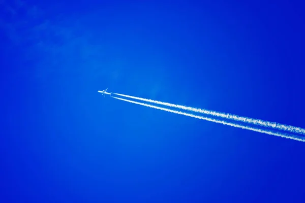 Um avião de passageiros voa contra um céu azul. Traço branco das turbinas da aeronave. — Fotografia de Stock