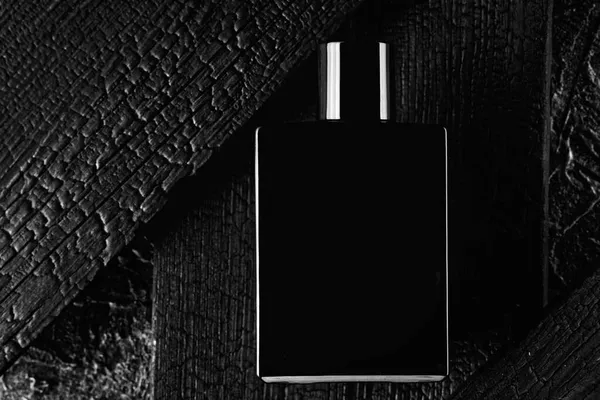 Αυτή είναι μια διαφημιστική φωτογραφία του eau de toilette ή άρωμα σε σκούρο στυλ.Μαύρο μπουκάλι στο φόντο ενός καμένου δέντρου — Φωτογραφία Αρχείου