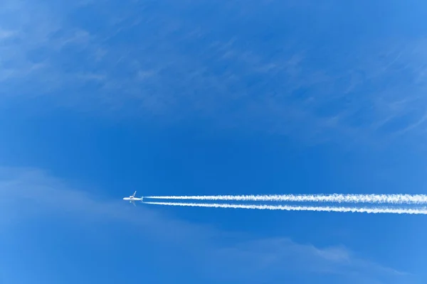 Um avião de passageiros voa contra um céu azul. Traço branco das turbinas da aeronave. — Fotografia de Stock