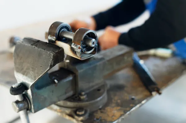 Un trabajador con overoles trabaja detrás de un banco de trabajo con vises de metal. Producción de piezas metálicas en la fábrica. — Foto de Stock