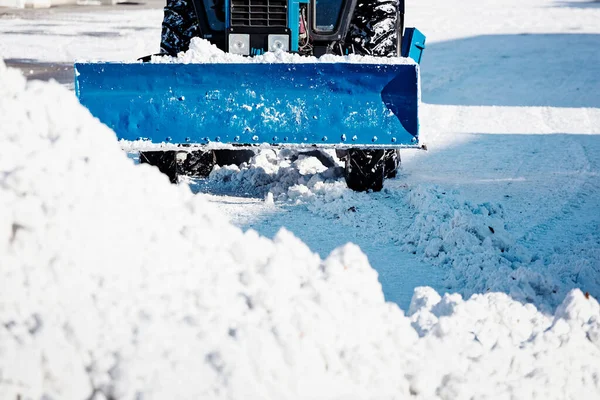 Un tractor azul con una pala limpia las calles de nieve en un día soleado de invierno. — Foto de Stock