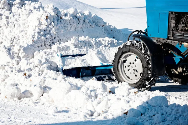 Un tractor de ruedas afuera pala nieve en una gran pila en un día soleado y helado. — Foto de Stock