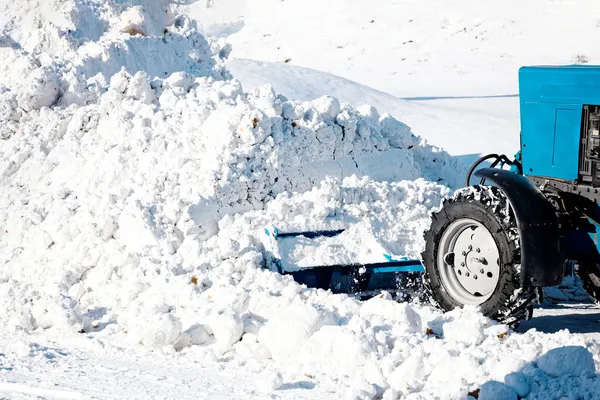 Un tractor de ruedas afuera pala nieve en una gran pila en un día soleado y helado. — Foto de Stock
