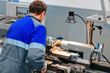 50-55 yaş arası bir yetişkin torna tezgahının arkasındaki atölyede çalışıyor. Metal parçalarının endüstriyel üretimi. Gerçek işçi..