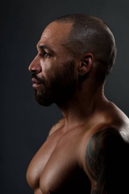 Kısa saçlı ve kaslı Latin Amerikalının vahşi portresi. Çıplak vücutlu güçlü bir adam başka tarafa bakıyor. Portre