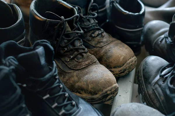 Many old work boots stand together. Old worn construction boots of workers. Real scene. Shift shoes.
