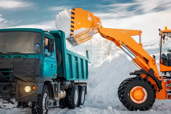 降雪和暴风雪后的除雪.挖掘机把雪装进卡车. 免版税图库照片