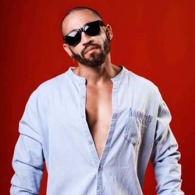 Tişörtlü ve güneş gözlüklü kendinden emin seksi adam kırmızı arka planda poz veriyor. Promosyon arka planı günlük giysiler.