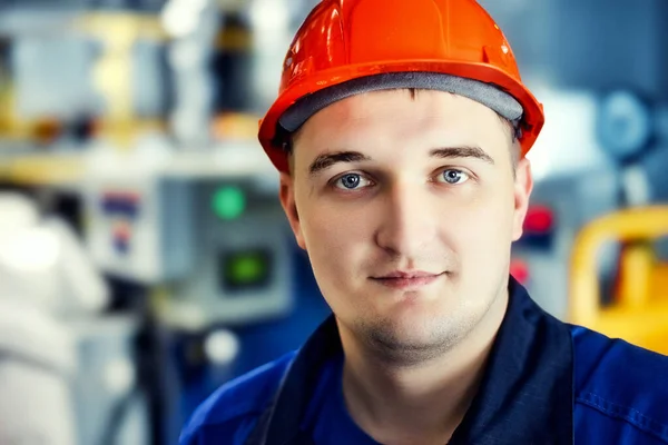 Retrato de joven ingeniero en casco en el entorno de trabajo en la factoría. trabajador de gas con confianza mira directamente a la cámara — Foto de Stock