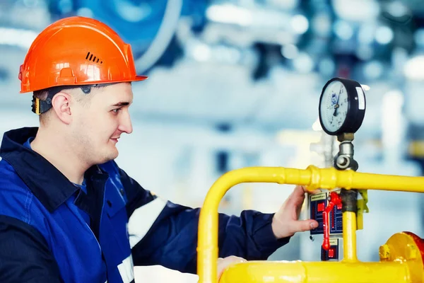 Operator of gas boiler house checks pressure on equipment. Portrait of engineer in helmet at work. Authentic scene workflow. working man in boiler room. Blurry background. Gasification and energy. Stockbild