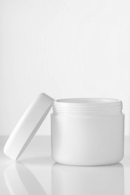 Boş beyaz krema kavanozu ya da kozmetik stantları beyaz camların üzerinde yansımalı açık kapaklı. Kopyalamak için alanı olan bir düzen.