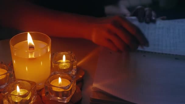 Geurkaarsen in kristallen kandelaars branden op tafel en de vrouw maakt aantekeningen in notitieboek.Moment van inspiratie voor auteur — Stockvideo