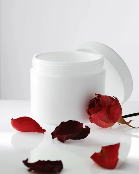 Κενό λευκό πλαστικό βάζο με καπάκι ανοιχτό στο φως φόντο. Πέταλα με κόκκινα τριαντάφυλλα. Αναζωογονητικά καλλυντικά. — Φωτογραφία Αρχείου