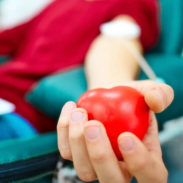 Topic of donation. Man donates blood in hospital. Mans hand squeezes rubber heart. Close-up. Donor sits in chair. — Zdjęcie stockowe