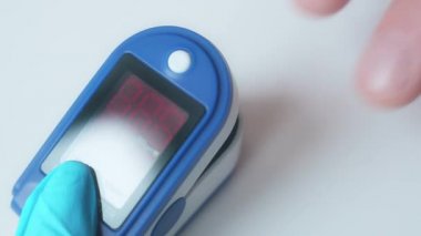 Yakın çekim video. Doktor, ekranlı elektronik cihazla parmak yoluyla doygunluğu ölçer. Sabit çerçeve.