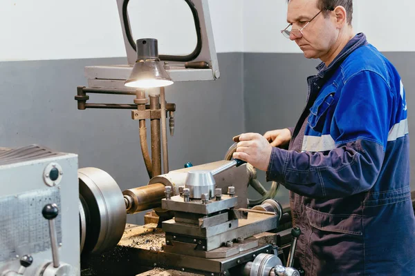 Turner adulto de 50-55 años trabaja en taller detrás del torno. Producción industrial de piezas metálicas. Trabajador real. — Foto de Stock