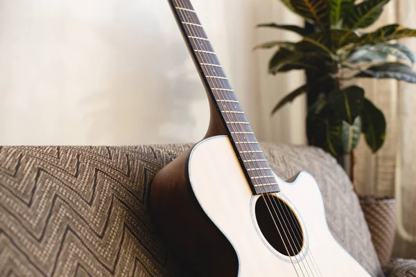 Odadaki kanepede akustik gitar duruyor. Geçmişi. Ev ortamında müzik aleti. — Stok fotoğraf