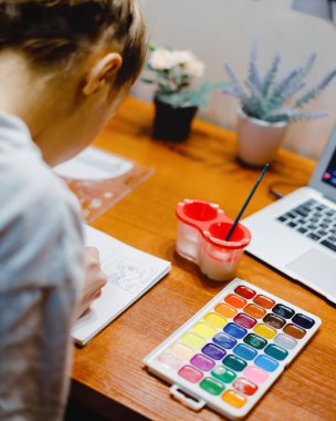 Genç kız odasında masada oturur ve suluboya boyalarla resim yapar. Yaratıcılık, ilham ve çizim teması.